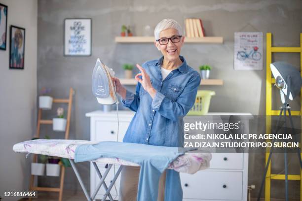 schöne reife seniorin mit grauen haaren bügeln ihre kleidung während der pandemie covid-19 . corona-virus. - ironing stock-fotos und bilder