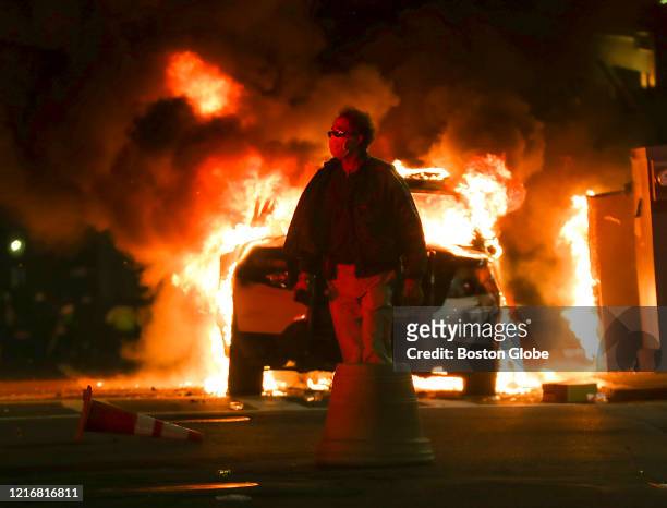 An unidentified man walks past a burning Boston Police car on Tremont Street in Boston on May 31, 2020 after a peaceful march from Dudley Square to...
