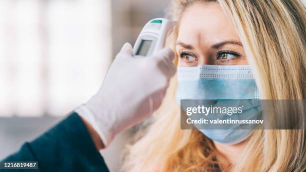 woman goes through a temperature checks before going to work in the office and wearing medical face mask during covid-19 - temperature checkpoint stock pictures, royalty-free photos & images