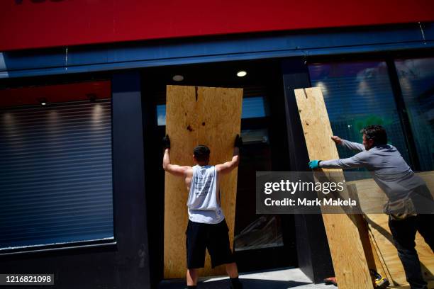 Max Beckmann and Bobby Brandimarte board up a damaged sporting goods store in the aftermath of widespread unrest following the death of George Floyd...