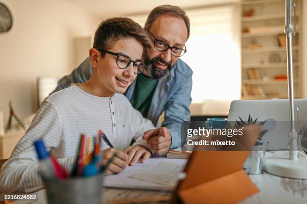 feliz padre ayudando a su hijo con la tarea - monoparental fotografías e imágenes de stock