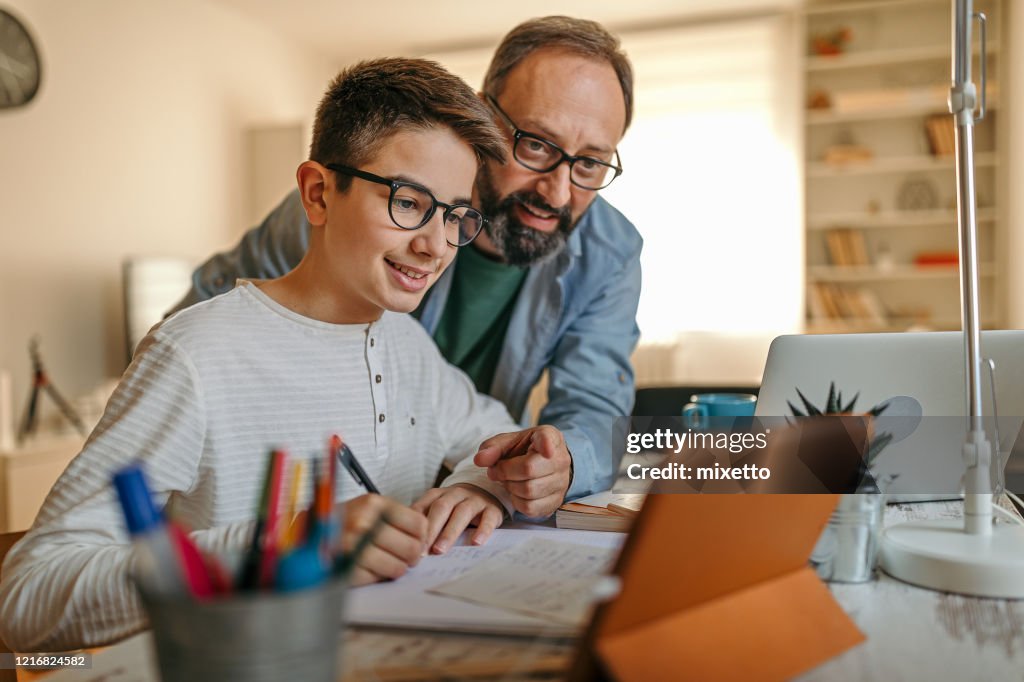 Gelukkige vader die zoon met thuiswerk helpt