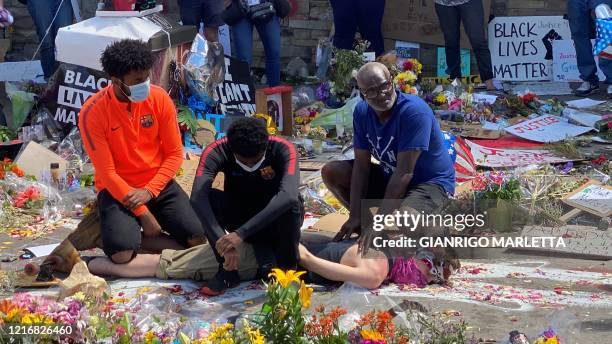 Three black men and a white man play the arrest of George Floyd at a makeshift memorial in Minneapolis, Minnesota on June 1, 2020. - A white man lies...