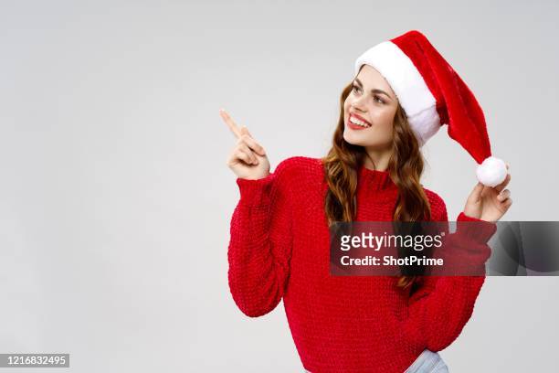 woman in christmas dress and santa claus hat shows her finger on an empty place on the banner - santa hat stock pictures, royalty-free photos & images