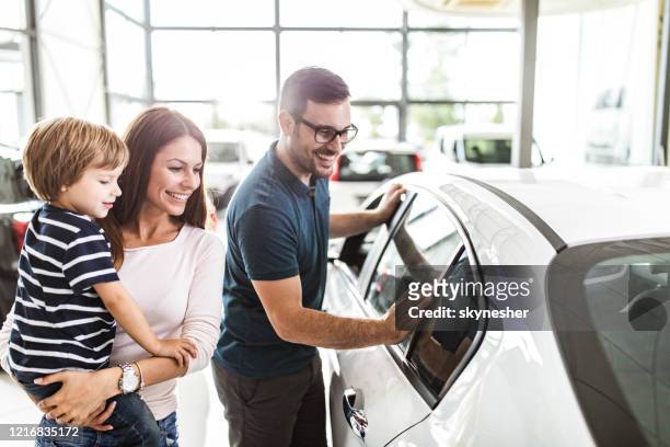 famiglia felice che sceglie un'auto nuova in uno showroom. - fare spese foto e immagini stock