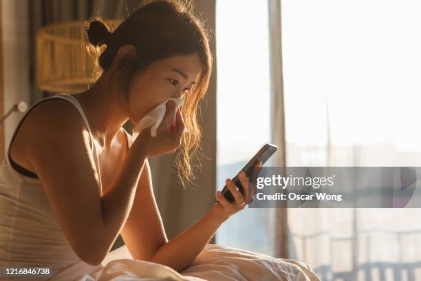 young woman sneezing while using mobile phone in bed - handkerchiefs people stock pictures, royalty-free photos & images