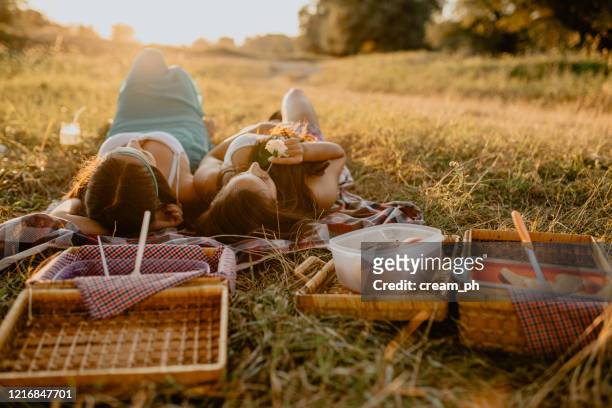 two women lying down on picnic blanket on a sunny day in nature - watermelon picnic stock pictures, royalty-free photos & images