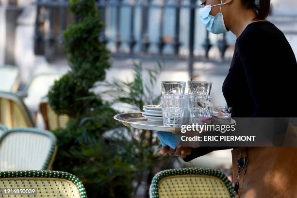 Waitress wearing a protective facemask carries a tray as she cleans the tables on the terrace of the "Cafe des phares", in place de la Bastille, in...