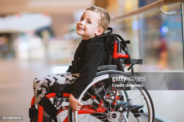 cute little boy in wheelchair in mall - wheelchair stock pictures, royalty-free photos & images
