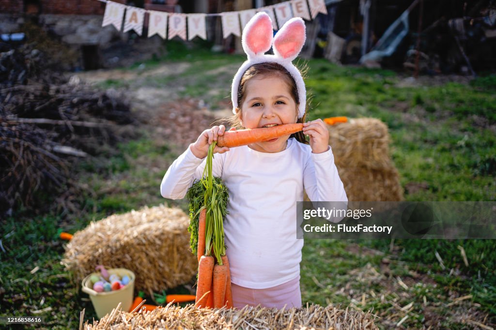 Cheerful child with rabbit ears costume biting a carrot during Easter