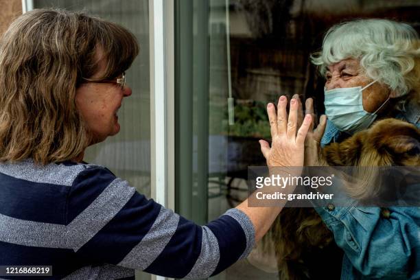 a daughter visiting her quarantined mother preventing contracting corona virus through the window - people social distancing stock pictures, royalty-free photos & images