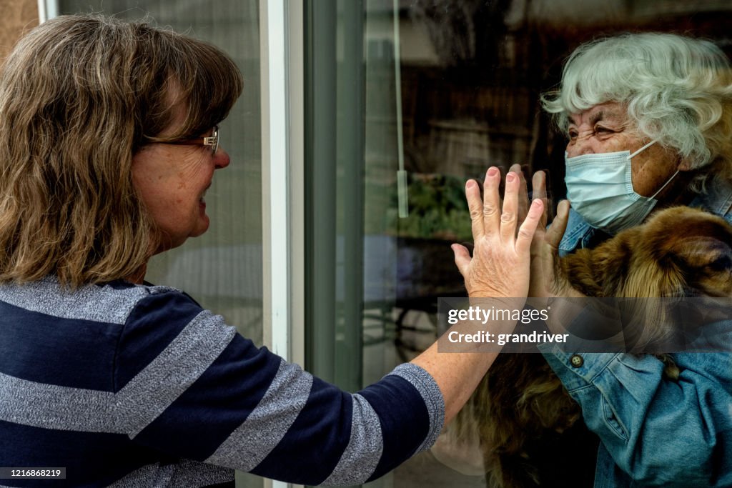 Uma filha visitando sua mãe em quarentena impedindo a contração do vírus corona através da janela