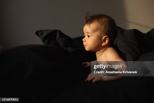 cute beautiful baby lying on black natural cotton bedding. portrait of crawling baby on the bed in his room. morning mood. - dark baby stock pictures, royalty-free photos & images