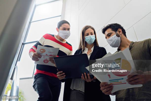 three coworkers are on the stairs of the company where they work with graphic documents and laptop all three wear masks - graphic accident photos stock pictures, royalty-free photos & images
