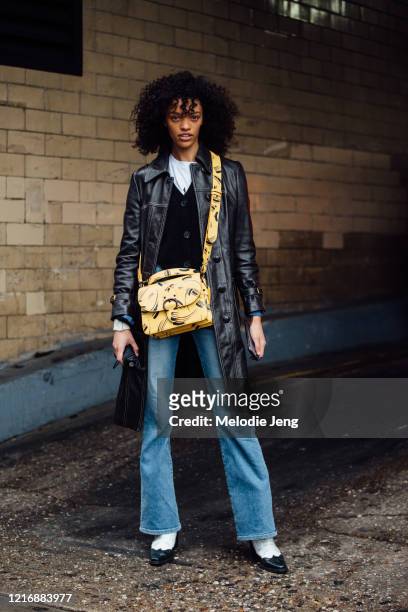 Model Kukua Williams wears a black leather coat, yellow print Coach bag, black cardigan, blue jeans, and black and white cowboy boots after the Coach...