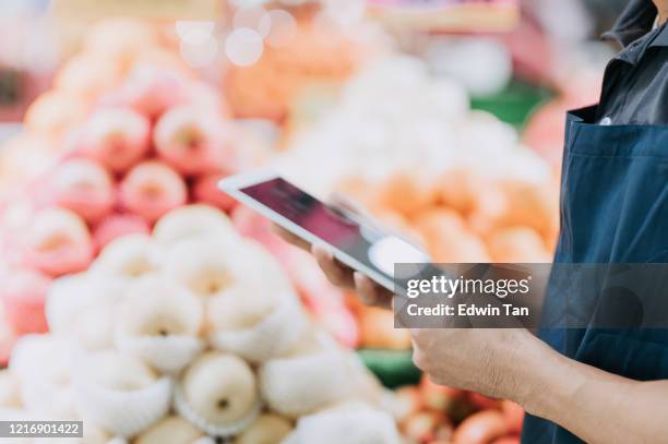 an asian chinese male store assistant checking inventory and price tag in front of fruit store department with his digital tablet - digital price tag stock pictures, royalty-free photos & images