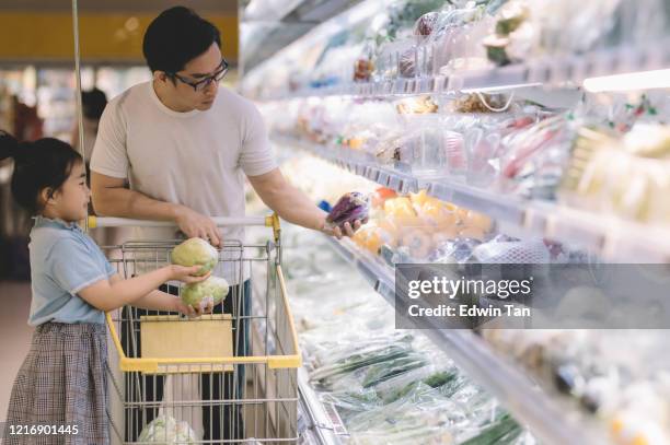 an asian chinese male buying fruit selecting them at refrigerated section vegetable store together with his daughter in supermarket - asian father and daughter stock pictures, royalty-free photos & images