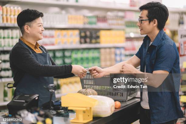 een aziatische chinese vrouwelijke kleinhandelsbediende kassier die creditcard van de klant tijdens controle bij kassierteller bij het gebruiken van creditcardscanner scant - convenience store counter stockfoto's en -beelden