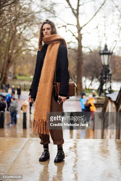 Model Veronica Manavella wears an oversized light brown cashmere scarf, black coat, brown pants, and black loafers after the Roksanda show during...