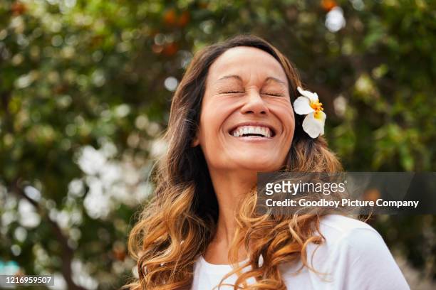 laughing mature woman standing outside with a flower in her hair - beautiful woman laughing stock pictures, royalty-free photos & images