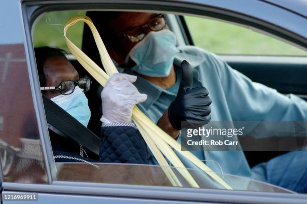 Couple hold up a palm leafs after attending a walk thru Palm Sunday Service at Friendship Baptist Church held due to the COVID-19 pandemic on April...
