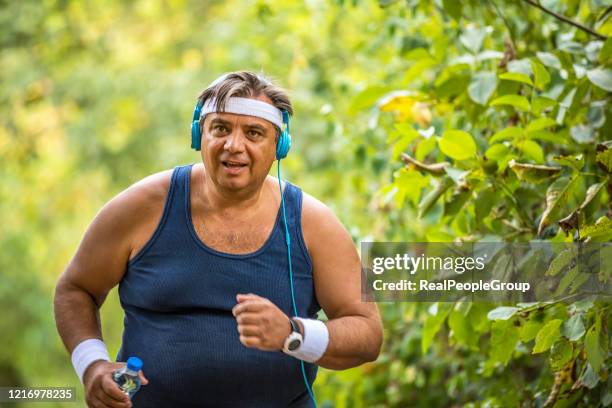 overweight man slowly running outdoors, active lifestyle as struggle with obesity - fat loss training stock pictures, royalty-free photos & images