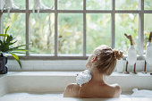 Young adult woman taking bath holding sponge in hand, washed shoulder