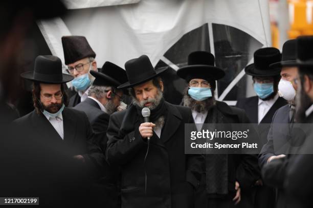 Man speaks as hundreds of members of the Orthodox Jewish community wearing face masks attend the funeral for a rabbi who died from the coronavirus in...