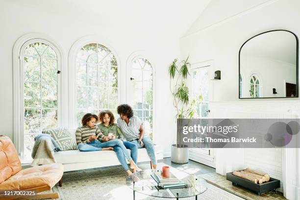 mother and daughters sitting in living room watching video on smart phone - beautiful barefoot girls imagens e fotografias de stock