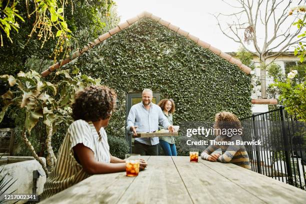 smiling father and daughter bringing food to family at picnic tablet in backyard - dish networks stock pictures, royalty-free photos & images