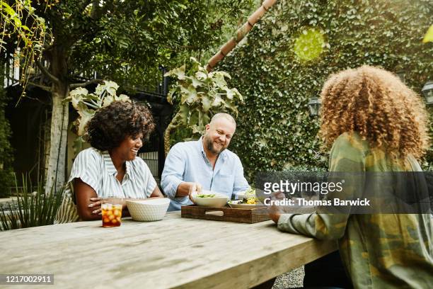 smiling family sharing meal at picnic table in backyard - picnic table stock-fotos und bilder