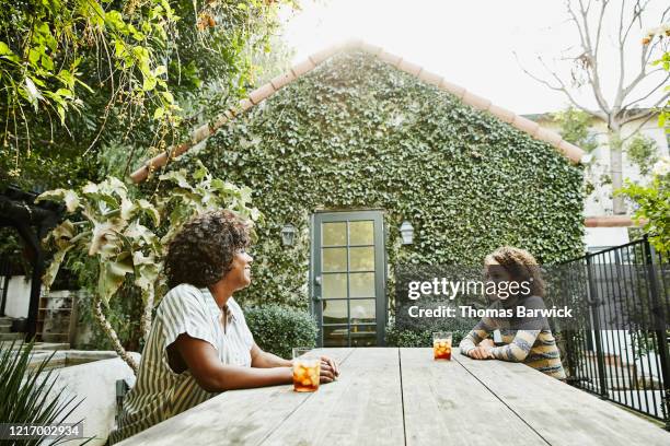 smiling mother and daughter sitting at picnic table in backyard - garden table stock-fotos und bilder