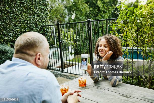 Smiling daughter showing photo to father on smart phone while sitting in backyard