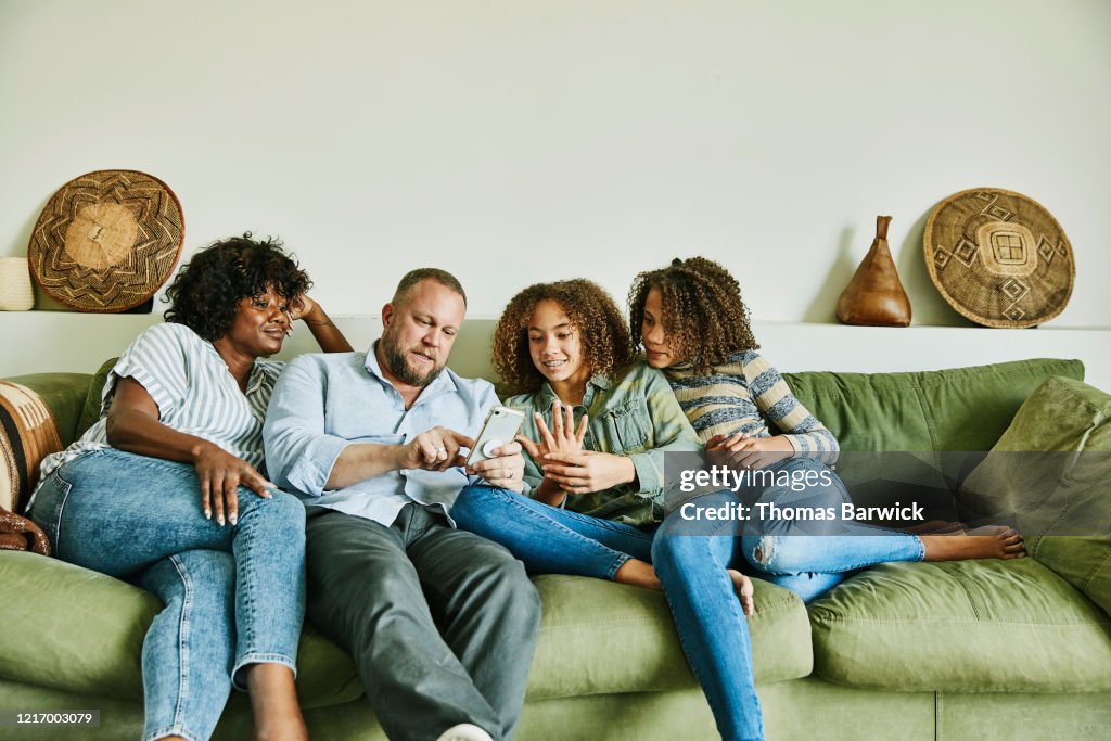 Family sitting on couch in living room looking at smart phone