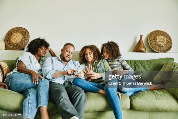 family sitting on couch in living room looking at smart phone - fille heureuse photos et images de collection