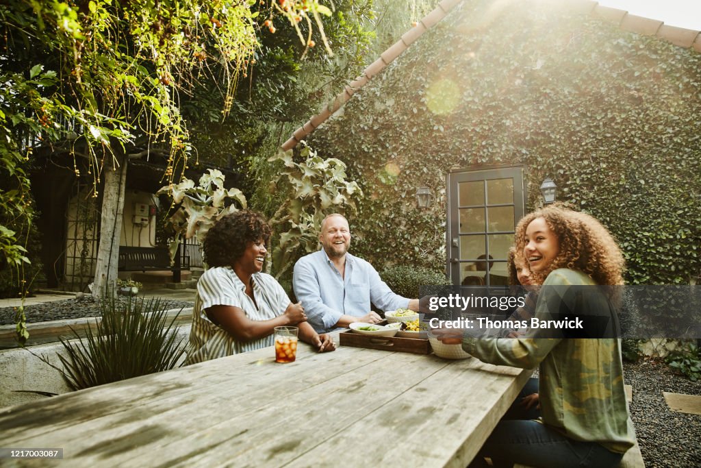 Laughing family sharing meal at picnic table in backyard