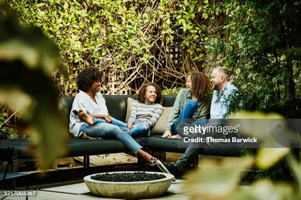 Smiling family hanging out by fire pit in backyard