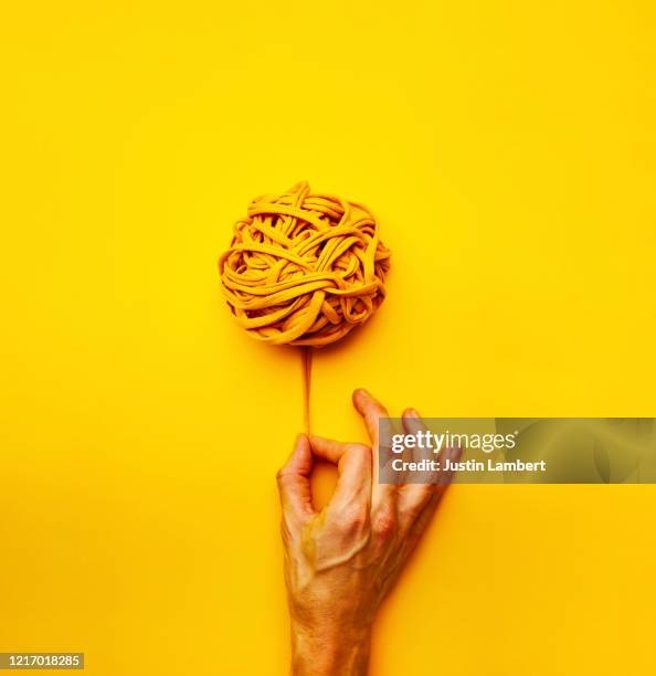 teasing out a thread from a ball of yellow yarn on a bright yellow backdrop - wollknäuel stock-fotos und bilder