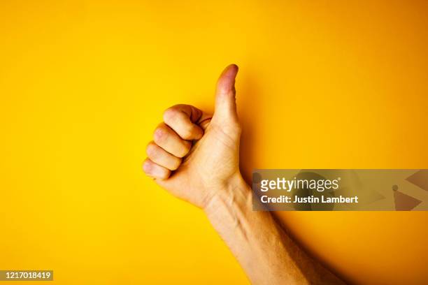 hand making the thumbs up signal on yellow backdrop - pulgar fotografías e imágenes de stock