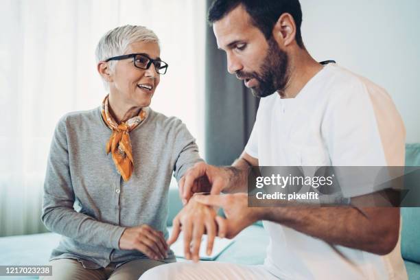 doctor examining senior woman's arm and wrist - rheumatism stock pictures, royalty-free photos & images