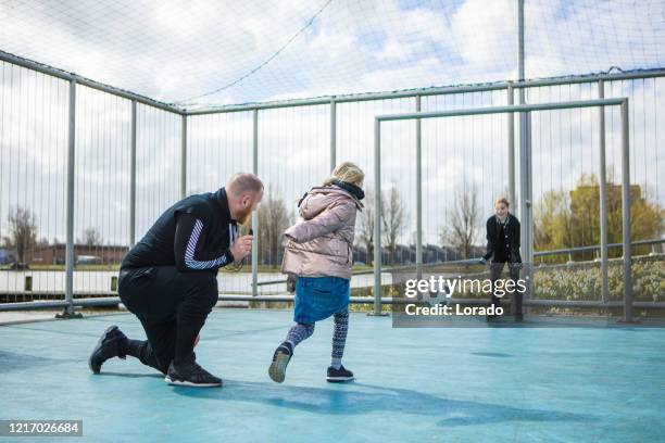 vader en dochters die voetbal in openlucht spelen - sportplaats stockfoto's en -beelden