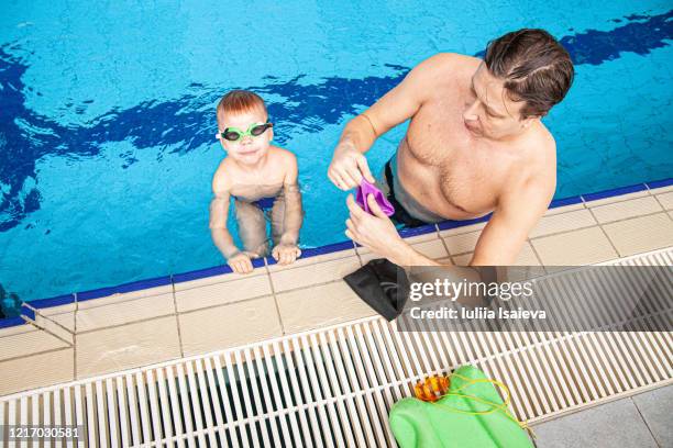 father putting on cap and goggles on son in pool - boy swimming pool goggle and cap stock pictures, royalty-free photos & images