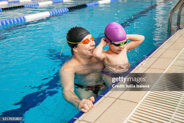 small boy preparing to swim with farther in lap pool - boy swimming pool goggle and cap stock pictures, royalty-free photos & images