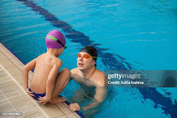 wet small boy talking with parent while sitting on poolside in modern sport complex - boy swimming pool goggle and cap stock pictures, royalty-free photos & images