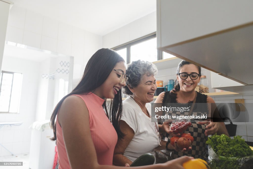 Grootmoeder, moeder en dochter die kruidenierswaren in de keuken uitpakken