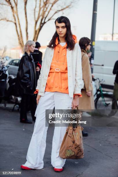 Model Margherita Tondelli wears a white jacket, orange hoodie, white cargo pants, a brown tote bag with sketches after the MSGM show during Milan...