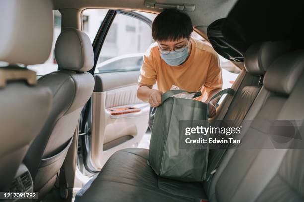 een aziatische chinese mid age vrouw het verwijderen van herbruikbare zakken uit haar auto die ze net kocht alle boodschappen uit de supermarkt met haar gezichtsmasker - chinese car home stockfoto's en -beelden