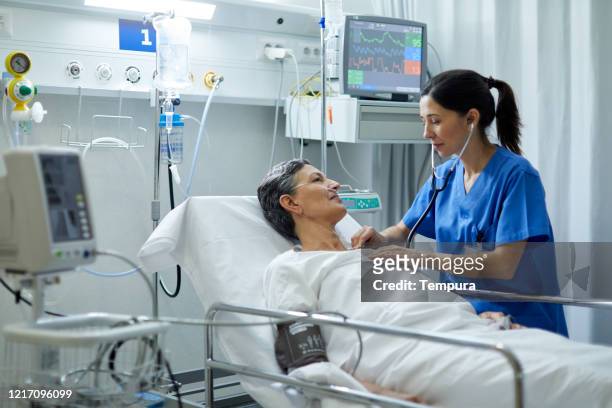 eine krankenschwester hört mit einem stethoskop das herz eines patienten. - icu patient stock-fotos und bilder
