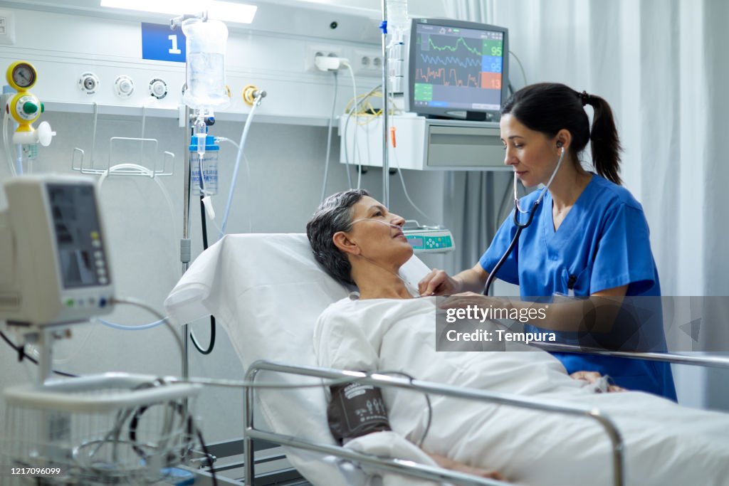 A female nurse is listening with a stethoscope the heart bit of a patient.