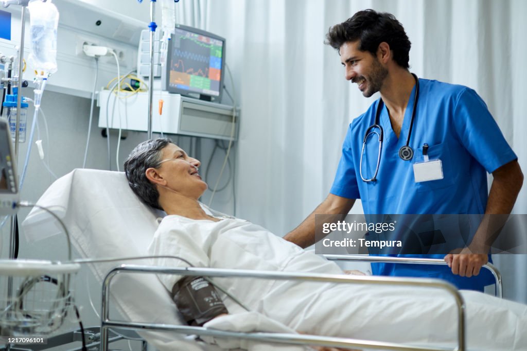 Une infirmière de sexe masculin écoute un patient dans la zone de rétablissement.